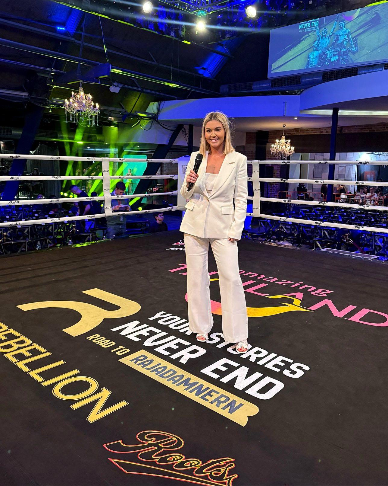 Teri Kearns holding a microphone in a boxing ring at a fight night, dressed in a white suit