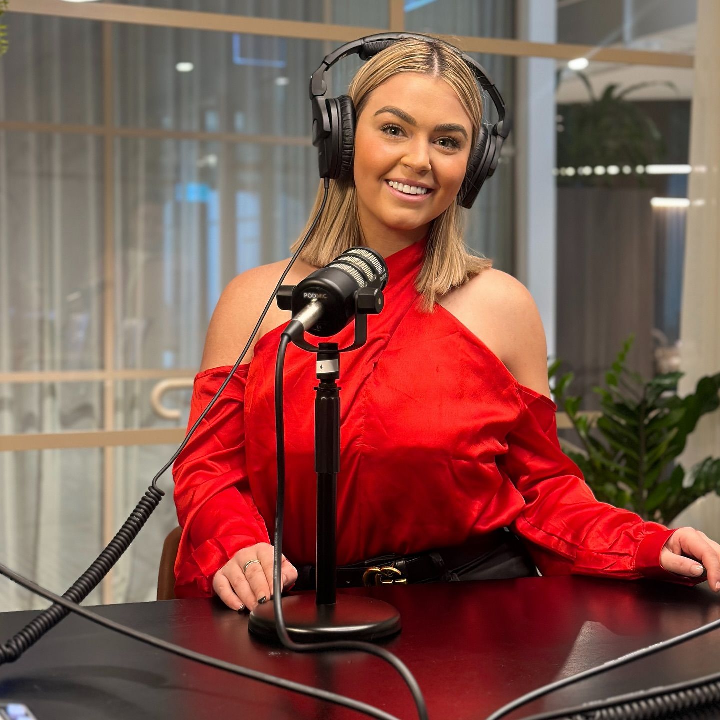 Teri behind a podcast microphone in a red outfit